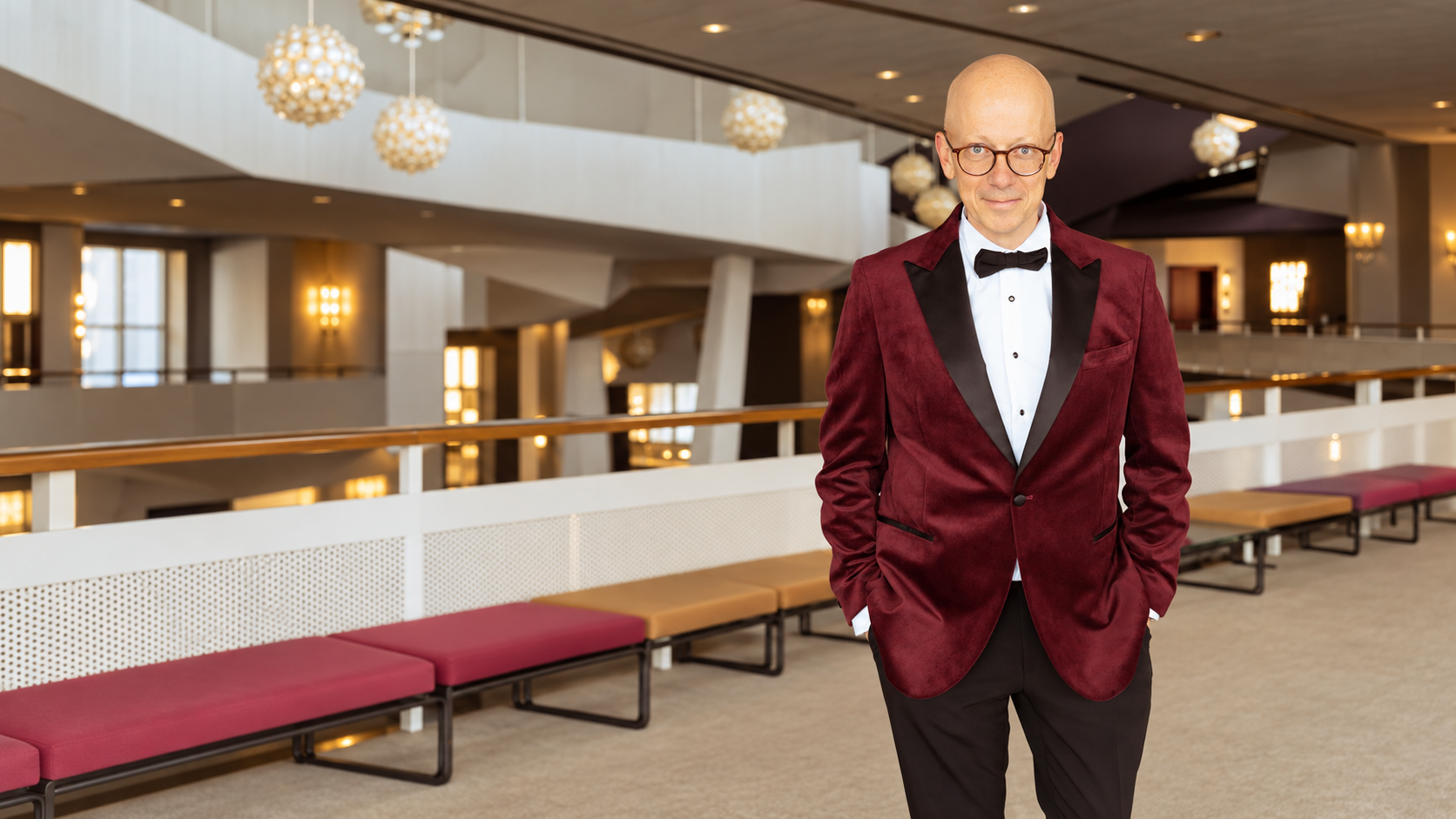 Simon Robinson steht im bordeauxroten Jackett in einem Konzerthaus